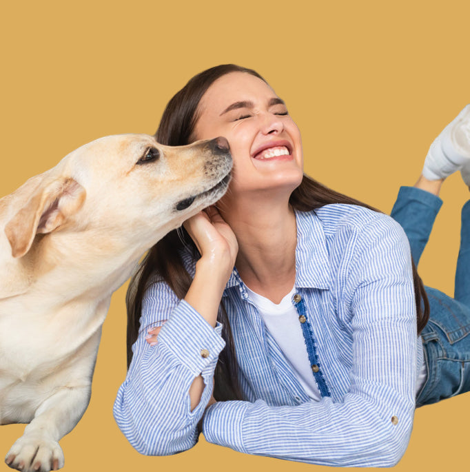 Woman lying on a bed with a dog licking her face, both appearing happy.